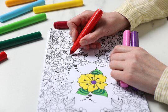 Woman coloring antistress picture with felt tip pen at white table, closeup