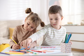 Fototapeta premium Little brother and sister drawing together at table indoors