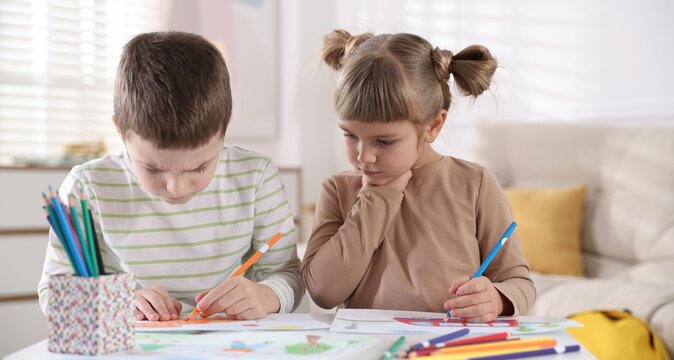 Little brother and sister drawing together at table indoors