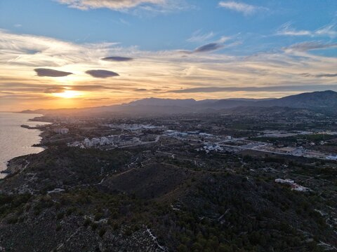 warm glow over shoreline and hills, dusk illuminates coast with shimmering waves and distant settlements