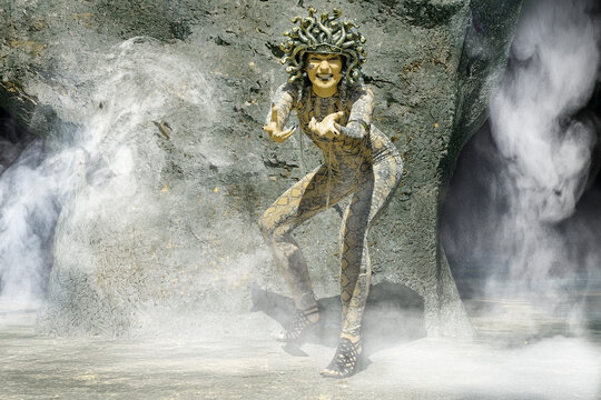 Eine Frau als Medusa verkleidet mit Schlangenkopf und Krallenh&auml;nden vor einer H&ouml;hle mit Nebel
