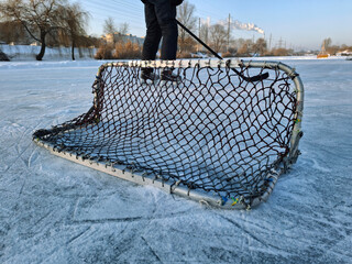 A hockey player stands on a frozen lake with a small goal