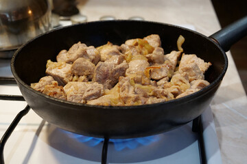 Frying meat. Pieces of meat with onion in frying pan on gas stove