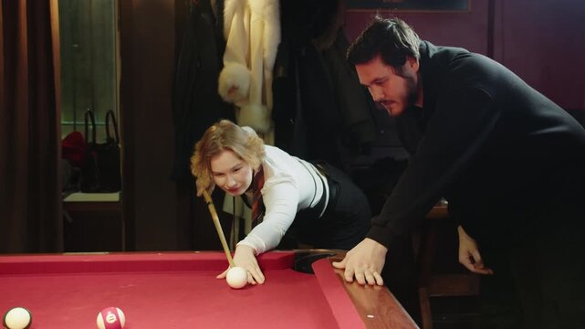 Young caucasian female player studies cue techniques from male instructor while casual game session. Youthful player engages in cue precision exercises alongside mentor in relaxed social venue