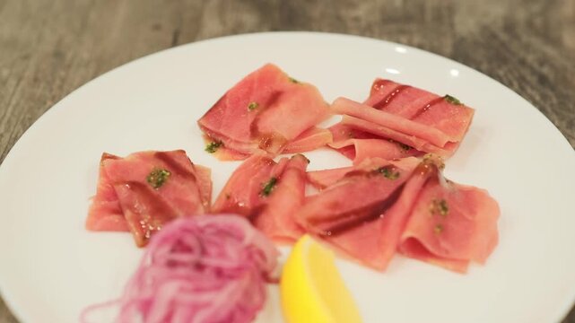 Tuna stroganina with lemon and onion slices on a white plate. Fresh raw fish dish for gourmet appetizer.