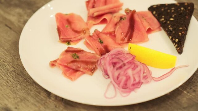 Tuna stroganina with pickled onion, lemon wedge, and rye bread on a white plate. Fresh seafood for gourmet dining, top view.