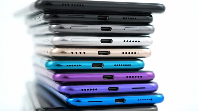 A close-up, studio-lit shot of a stack of smartphones, showcasing their colorful bottom ports against a clean white background.