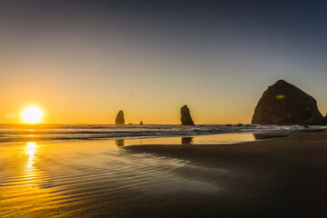 The sun is setting over the ocean, casting a warm glow on the beach
