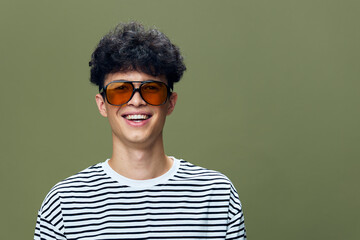 smiling man wearing striped shirt and oversized sunglasses with curly hair on green background, cheerful and youthful expression