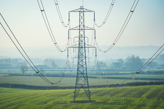 Sun setting behind the electric power lines running from Dungeness power station on the Kent coast south east England UK