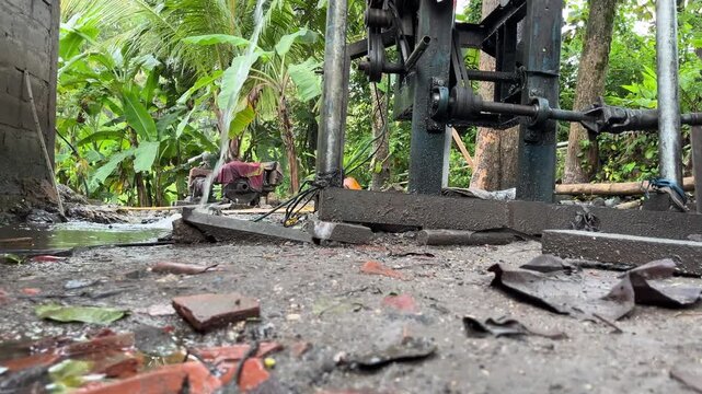 Close ground perspective of drilling machine structure with wet surface and scattered debris. Rural water well drilling and infrastructure development concept.