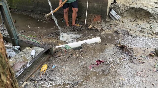 Worker handling water flow in muddy ground area near construction or drilling site. Water management activity in rural environment during wet conditions.