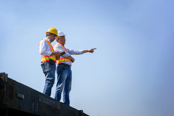Senior engineers standing on a platform, pointing towards the future of a large-scale industrial project, Site managers in hardhats discussing project development and surveying the construction area