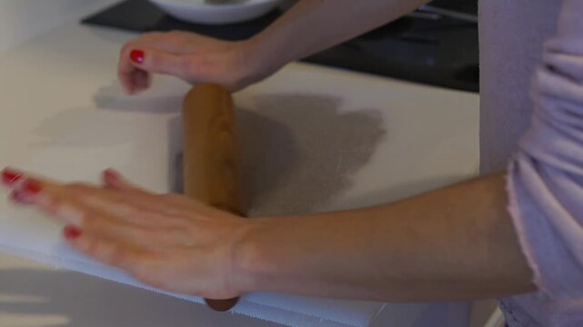 Close-up of hands using a traditional wooden rolling pin to flatten dough between sheets of parchment paper for a professional and clean baking result.