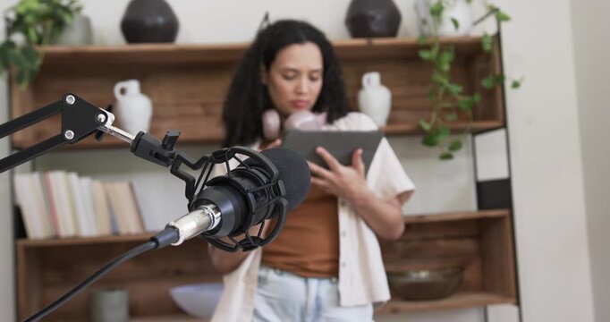 Female host wearing headphones scrolling tablet and smiling, mic leading content review in studio