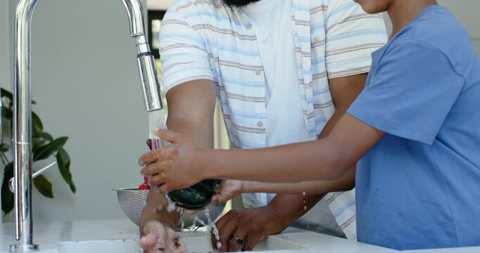 African American father and youth son turning faucet, rinsing squash and colander for cooking