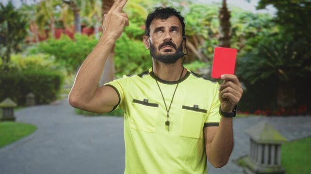 Referee man wearing yellow shirt and whistle holding red card and pointing finger to temple on street; authority discipline frustration.