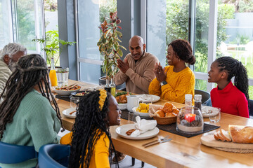Multigenerational African American family clapping and sharing turkey at dining table near windows