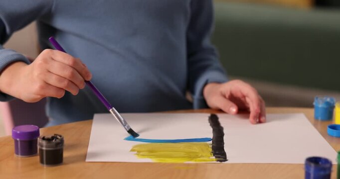 Little girl drawing with brush and paints at wooden table indoors, closeup. Camera moving left and forward