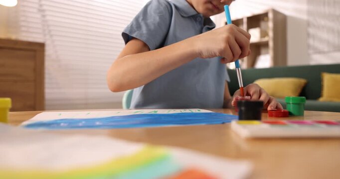 Little boy drawing with brush and paints at table indoors, closeup