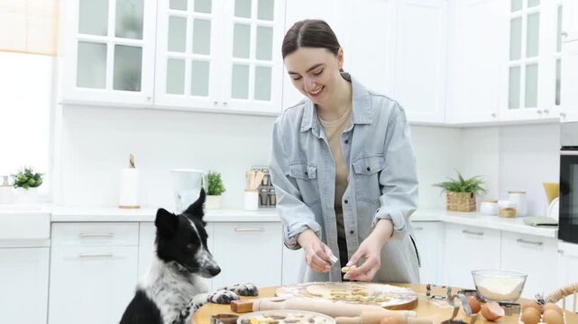 Woman making cookies near cute dog at wooden table in kitchen. Camera moving forward