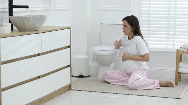 Pregnant woman suffering from nausea over toilet bowl in bathroom. Toxicosis during pregnancy