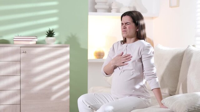 Pregnant woman suffering from nausea on sofa indoors. Toxicosis during pregnancy