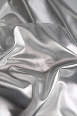 Close-up of silver satin fabric with soft flowing folds and smooth reflective texture. The metallic sheen and elegant draping create a luxurious abstract background suitable for product mockups, brand