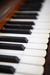 Selective focus close-up of black and white piano keys with soft depth of field and warm wooden tones. The diagonal composition and blurred background create a moody, artistic perspective ideal for mu