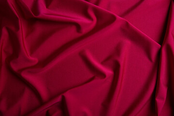 Close-up of red satin fabric with soft flowing folds and smooth reflective texture. The metallic sheen and elegant draping create a luxurious abstract background suitable for product mockups, branding