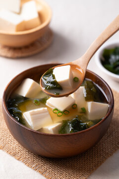 Healthy Japanese miso soup with soft tofu and seaweed in a wooden bowl being scooped with a spoon