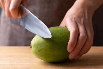 Close up of hand holding knife and cutting green mango on wooden board