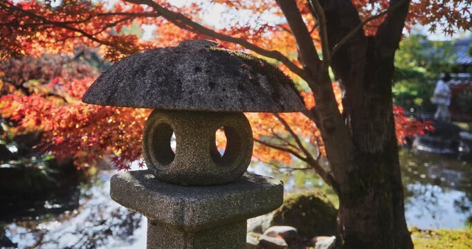 Closeup on stone Japanese lantern in front of autumn trees - steady cam shot