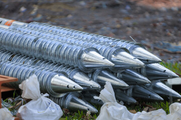 Stack of shiny metal ground screws with pointed ends is neatly arranged on grass, ready for construction use. background is slightly blurred, highlighting screws metallic texture © pirom