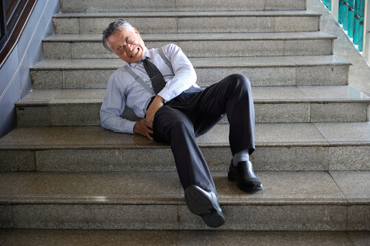 Senior man falling down the stairs, in pain and distress. He is wearing formal attire, and is on a set of stairs