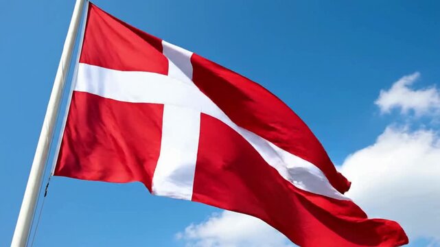 The national flag of Denmark, known as Dannebrog, waving proudly against a bright blue sky with scattered white clouds.