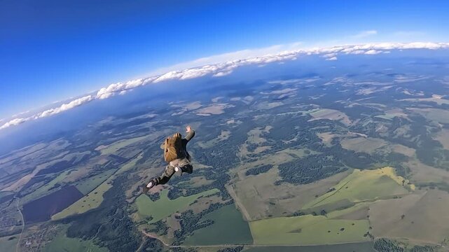 A skydiver freefalls over fields and forests under a bright blue sky. Extreme, adrenaline, active recreation, adventure, aerial views.
