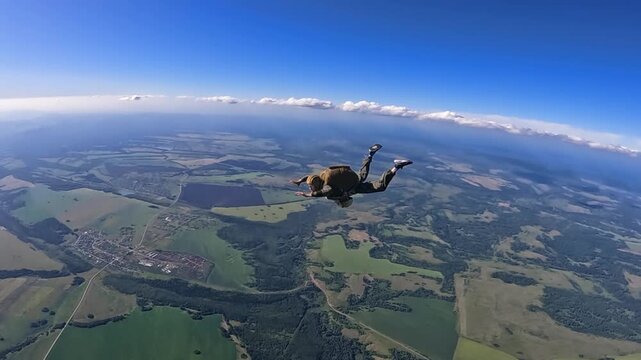 A parachutist freefalls over a rural landscape of fields and forests. Wide-angle, high altitude, extreme, clear sky and clouds.
