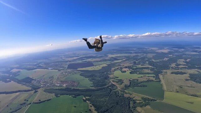A parachutist freefalls against a backdrop of blue sky and clouds over fields and forests. Extreme sport, heights, a sense of freedom.
