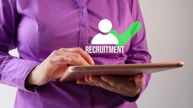 Close-up of a businesswoman interacting with her tablet, displaying an animated avatar icon, a checkmark, and the word "Recruitment." Finding the right staff.