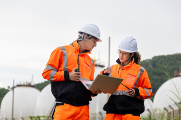Professional technical team in safety uniforms using a laptop to coordinate operations at natural gas storage facility, Engineers performing a site inspection and safety audit at a fuel terminal