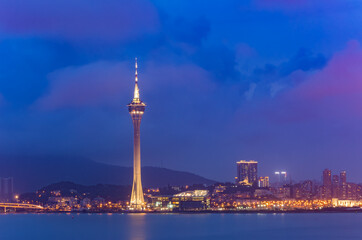 Fototapeta premium Macau tower illuminated against twilight sky over cityscape.