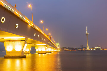 Obraz premium Golden bridge lights reflect on calm waters at dusk.