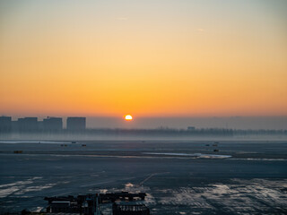 Naklejka premium Sunset glows over frozen airport tarmac at dawn.