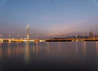 Fototapeta premium Macau tower illuminated at twilight over calm waters.