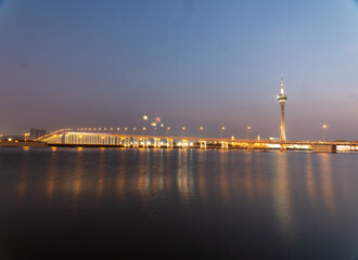 Fireworks explode over illuminated bridge and tower at dusk.