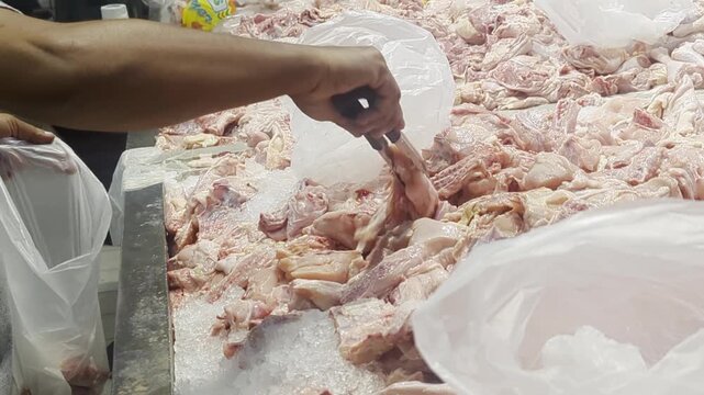 A person using metal tongs to pick raw chicken pieces from a fresh meat display at a supermarket market stall.