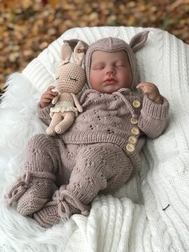 Realistic reborn baby doll sleeping on soft white fur, wearing handmade knitted outfit in natural light