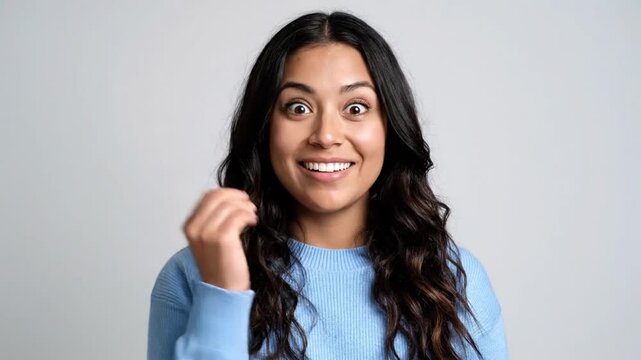 A young woman with long dark hair expressing excitement and happiness with a bright smile and a clenched fist near her face