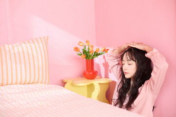 ピンク背景の部屋でリラックスするアジアの若い女性のポートレート